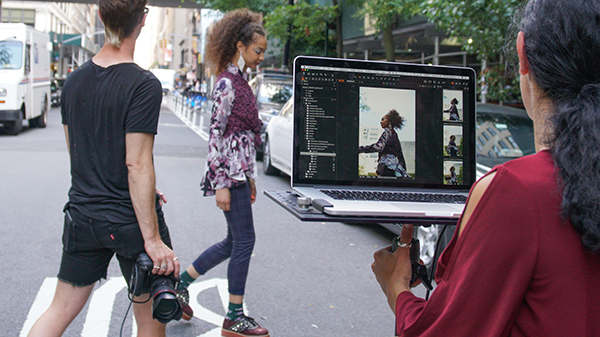 a student photographer takes photos of a model while students look at the photos on a laptop